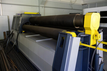 Naklejka premium Close-up of a robust metal rolling machine with large cylindrical rolls. Bright yellow safety components contrast with dark steel and blue-gray machinery. Scene conveys industrial strength, precision 