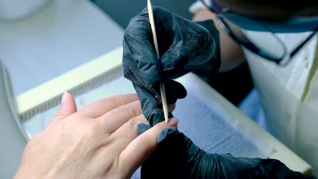 Finger nail treatment, fashion, manicure making process in beauty salon Electric nail file drill in action, close up of beautician hands in black gloves working on client fingernails.