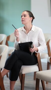 Young woman in an elegant gray dress sits in a classroom and listens to a lecture and refresher training, she takes notes on a modern tablet.