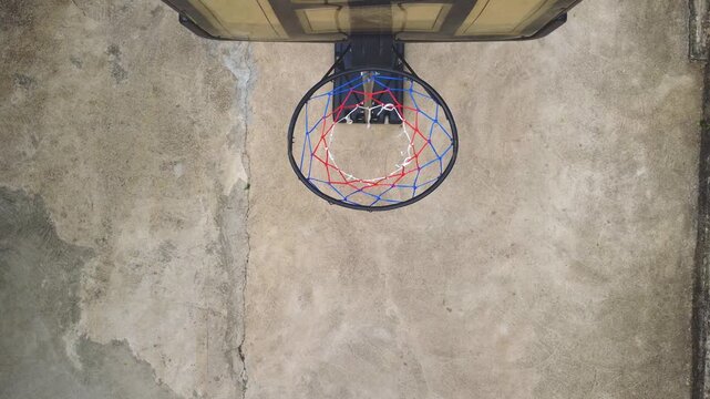 Top-down aerial shot capturing a basketball dropping through the hoop net on an outdoor concrete court. The unique bird's-eye perspective highlights the precise moment of scoring, ideal for  basketbal