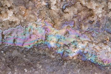 Fototapeta premium Iridescent oil stain creating a colorful rainbow sheen on melting dirty spring snow, showing environmental pollution and chemical waste runoff on the city road surface during seasonal thaw