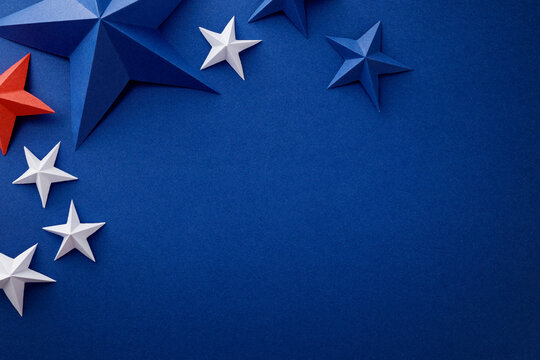 Festive arrangement of red, white and blue paper stars and curled ribbons on dark blue background. Patriotic border with empty space for text, suitable for Independence, Fourth of July, Memorial