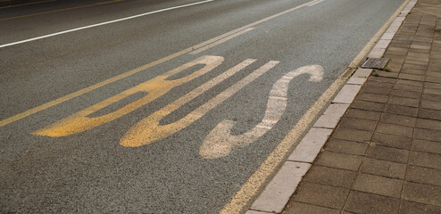 Fototapeta premium Bus lane marking painted on an urban roadway beside a sidewalk. Concept of public transport, traffic management and city infrastructure.