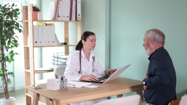 Adult physician sits at desk with elderly man patient, conversing about health concerns and explaining treatment options