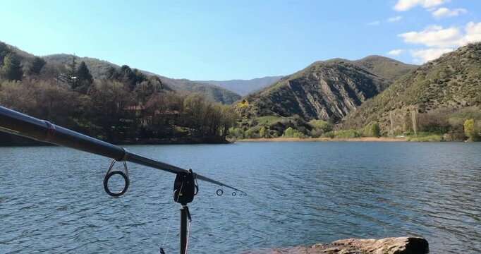 Fishing rod setup by a serene mountain lake on a clear sunny day