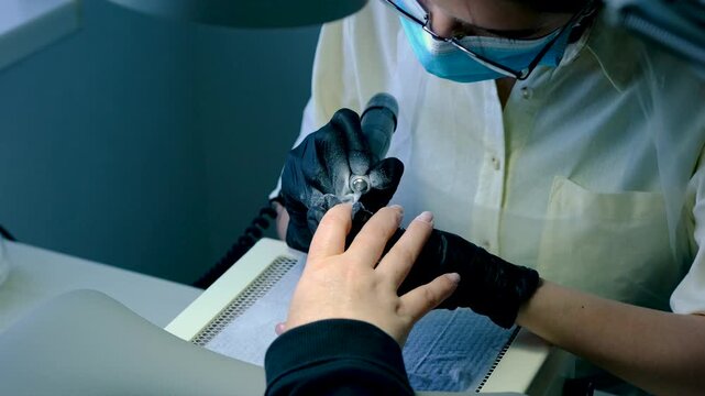 Finger nail treatment, fashion, manicure making process in beauty salon Electric nail file drill in action, close up of beautician hands in black gloves working on client fingernails.