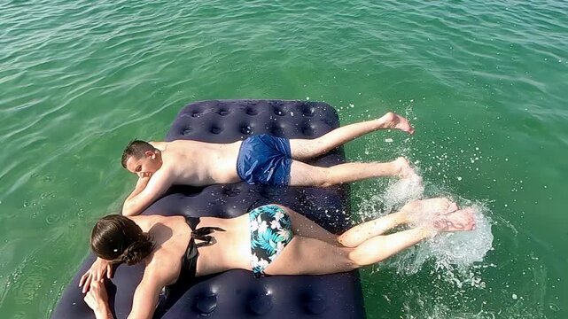 Couple enjoying summer vacation lying on air mattress and leg splashing in slow motion