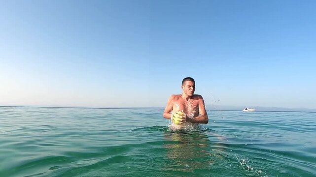 Man playing catching ball in clear sea water under sunny sky, slow motion