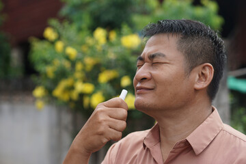 Fototapeta premium Close-up of a man inhaling a herbal inhaler outdoors with eyes closed, enjoying a refreshing sensation, concept of traditional wellness, natural remedy, relaxation and self care