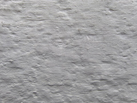 Textured white rendered plaster wall surface with hand-applied trowel marks and irregular surface relief. Close-up detail of lime or cement render showing horizontal stroke patterns.