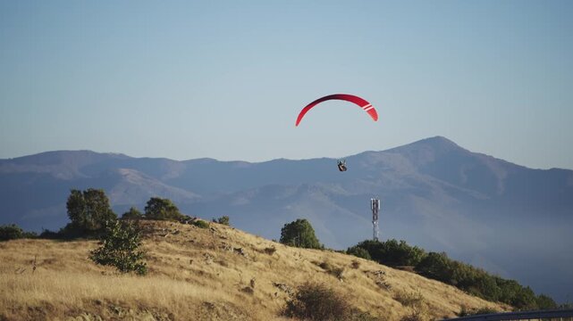 Solo paraglider hovers gracefully against a clear sky, supported by a striking red parachute