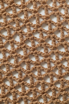 Close-up of beige handmade crochet textile featuring a repeating lace pattern and delicate openwork texture, ideal for craft, sewing, and fabric background use.