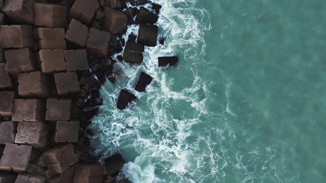 Cinematic 4K aerial drone captures waves breaking against the rocky breakwater at Miramar Beach in Ciudad Madero, Tamaulipas, with calm turquoise water stretching beyond the rocks under natural daylig