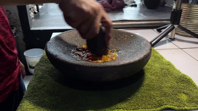 Close-up of hand grinding fresh red chilies in a stone mortar to make sambal paste.  
A detailed stock footage clip showing a person's hand using a stone pestle to grind and crush fresh red hot chilli