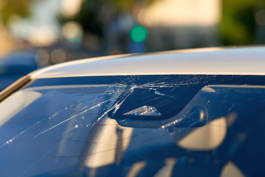 Damaged car front windshield, severe crack patterns, auto glass replacement and repair needed, transportation safety and insurance claim. Cracked windshield glass with spiderweb fracture patterns