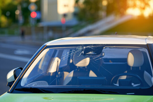 Parked car with broken windshield glass with spiderweb cracks spreading from impact point, auto repair, replacement service needed, vehicle damage and transportation safety concern. Car window repair