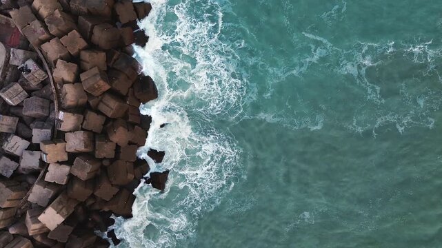 Cinematic 4K aerial drone captures waves breaking against the rocky breakwater at Miramar Beach in Ciudad Madero, Tamaulipas, with calm turquoise water stretching beyond the rocks under natural daylig