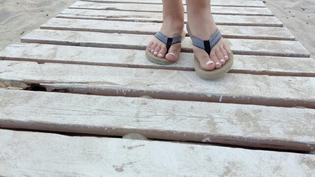 Close-up of a woman walking on a wooden boardwalk at the beach