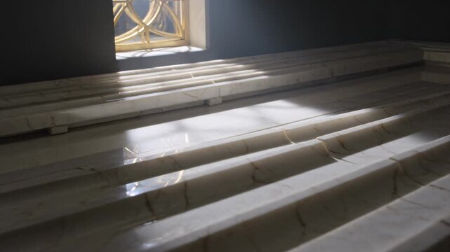 Sweeping sunlight from small window moving across marble tiers in chapel, casting gold grille glow