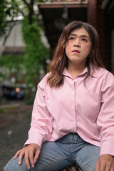 Naklejka premium Transgender Thai Isan woman looking away thoughtfully while sitting on an outdoor bench
