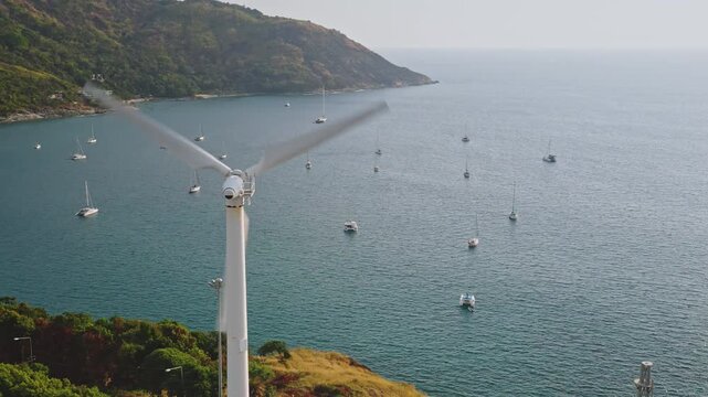 Wind turbine spinning its blades, generating renewable clean energy for the island, symbolizing sustainable development and ecological solutions while sailboats are anchored in the calm blue ocean
