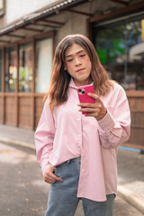 Fototapeta premium Transgender Thai Isan woman texting on her pink smartphone while standing outdoors
