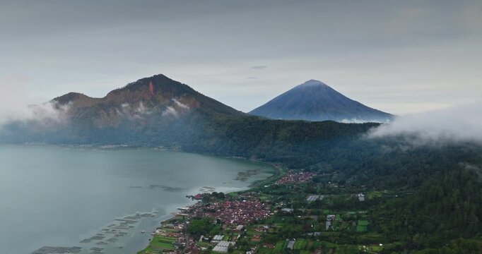 Mount Batur and Lake Batur forming a caldera while low clouds covering the sides of Mount Batur with Mount Agung rising from the mist in Kintamani, travel and explore Bali. Aerial view drone flight