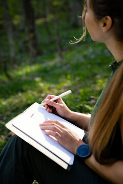 Young woman recording thoughts and ideas in a notebook surrounded by nature. Concept of wellbeing, creativity and mindful living.