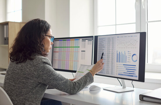 Accountant analyst woman at office monitors audit data. She reviews spreadsheets on computer screens, verifies finance and runs analytics for compliance. Concept shows finance reports analysis.