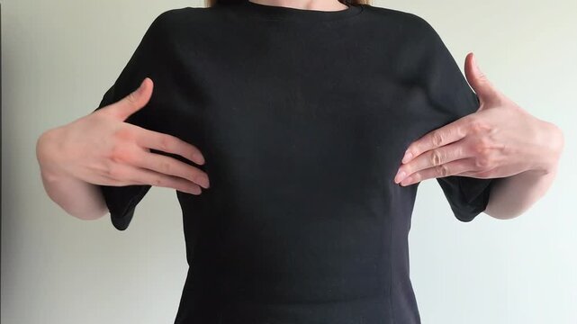 Woman performs self breast examination checking for lumps with both hands. She palpates her chest carefully feeling for any unusual changes. Concept of breast cancer awareness, self check