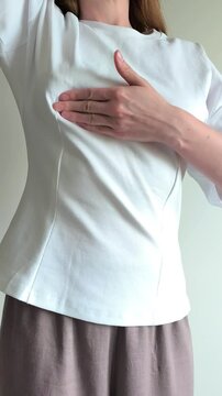 Woman performs a breast self examination feeling for lumps with her hand. She checks her chest carefully searching for any unusual changes. Concept of breast cancer awareness, self check and