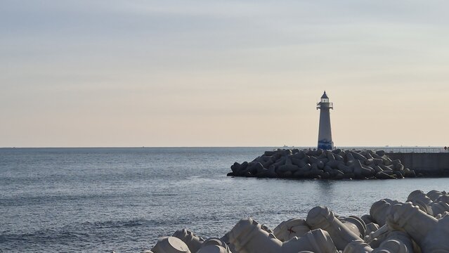 Vertical shot of a beautiful white lighthouse standing on the breakwater with calm ocean background