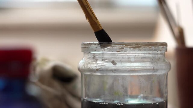 Close-up of an artist washing paint residue from his brush in a jar of water