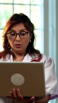 Indian lady doctor and female patient discussing case on laptop during detailed consultation in modern clinic, showing senior expertise, digital healthcare workflow, patient focused medical guidance