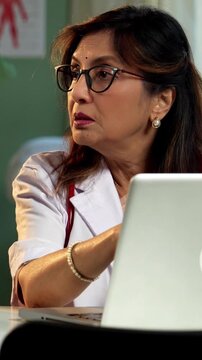 Indian lady doctor and female patient discussing case on laptop during detailed consultation in modern clinic, showing senior expertise, digital healthcare workflow, patient focused medical guidance