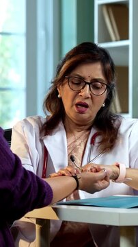 Experienced Indian lady doctor woman checking young female patient in clinic using stethoscope, torch and pulse examination during routine health checkup in modern medical facility