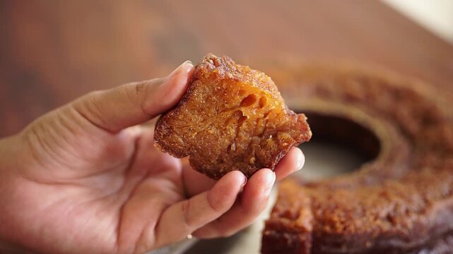 Close up of hand pressing a slice of Sarang Semut cake to show its soft and chewy texture