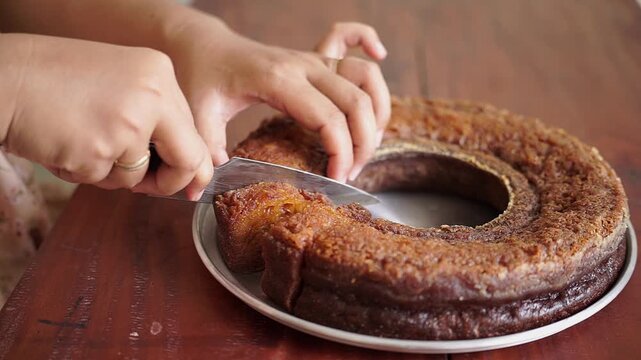 Close up of woman slicing homemade caramel cake or Sarang Semut cake on wooden table. Traditional Indonesian honeycomb cake with soft texture