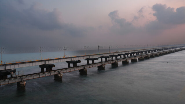 A scenic view of Pamban railway bridge over the sea near Rameswaram in Tamil Nadu, India, captured during soft evening light with cloudy sky and calm ocean water.