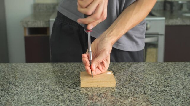Close up man screwing a screw into a wooden board with screwdriver with clear sound. Hands working on wood. Carpentry, DIY repair, construction and ASMR concept.
