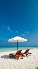 Fototapeta premium Two wooden lounge chairs under a white umbrella on a pristine sandy beach by the ocean