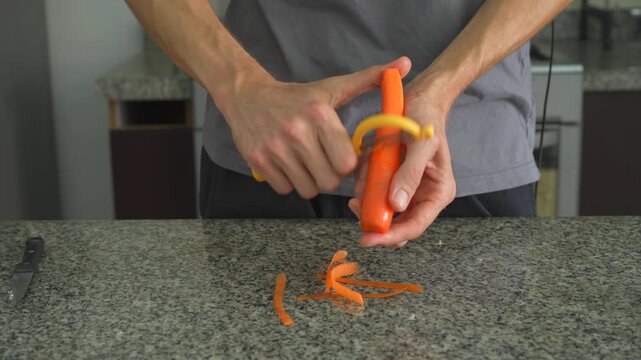 Close up man peeling carrot with vegetable peeler with clear sound. Hands preparing fresh ingredient on cutting board. Cooking preparation, kitchen routine and ASMR concept.