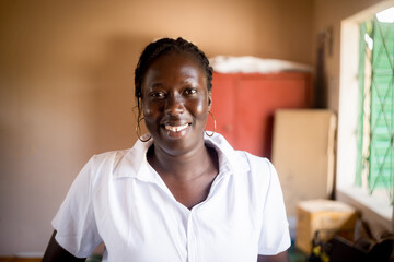 Obraz premium Portrait of smiling young african business woman sitting at desk in office writing and working in team on laptop,corporate jobs and economy in africa