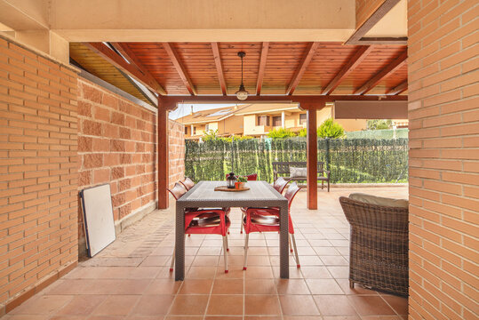 A modern terrace with a polished cement floor, an aluminum pergola, a portable barbecue, and a corner with aromatic plants in ceramic pots.