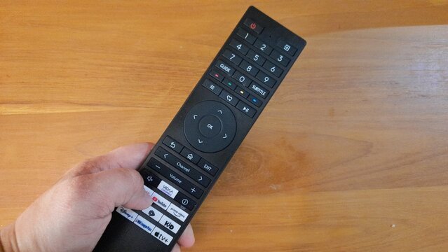 Banyuwangi, East Java, Indonesia - April 29 2026. Hand holding a black TV remote control with smart TV buttons