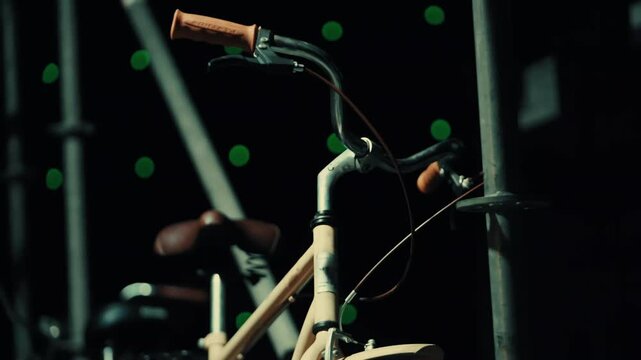Close-up bicycle handlebars with brown grips. Metal tubes glow softly. Green bokeh lights shimmer in the background. Wooden frame shows rustic texture. Scaffolding pipes stand tall