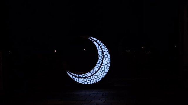 a silhouette of a blue crescent moon shaped lamp decoration that glows brightly in the darkness. religious concept