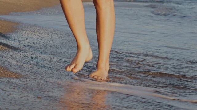Low angle shot of an 11 year old boy walking barefoot on wet sand, with gentle sea waves washing over his feet. Summer family vacation concept in Kato Gouves, Crete, Greece