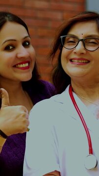 Indian woman doctor with young female patient smiling and looking at camera outdoors, showing positive healthcare interaction, patient satisfaction, recovery, happiness, and senior medical expertise