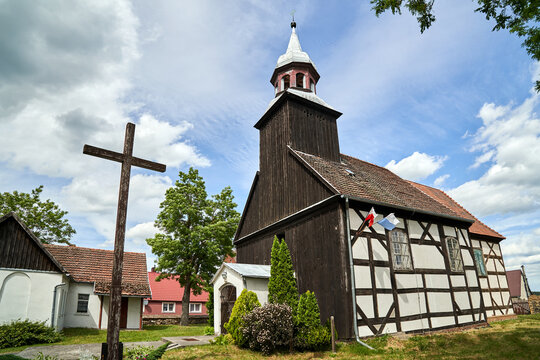 Wooden cross in front of the historic parish church with a bell tower in the village of Kalsko